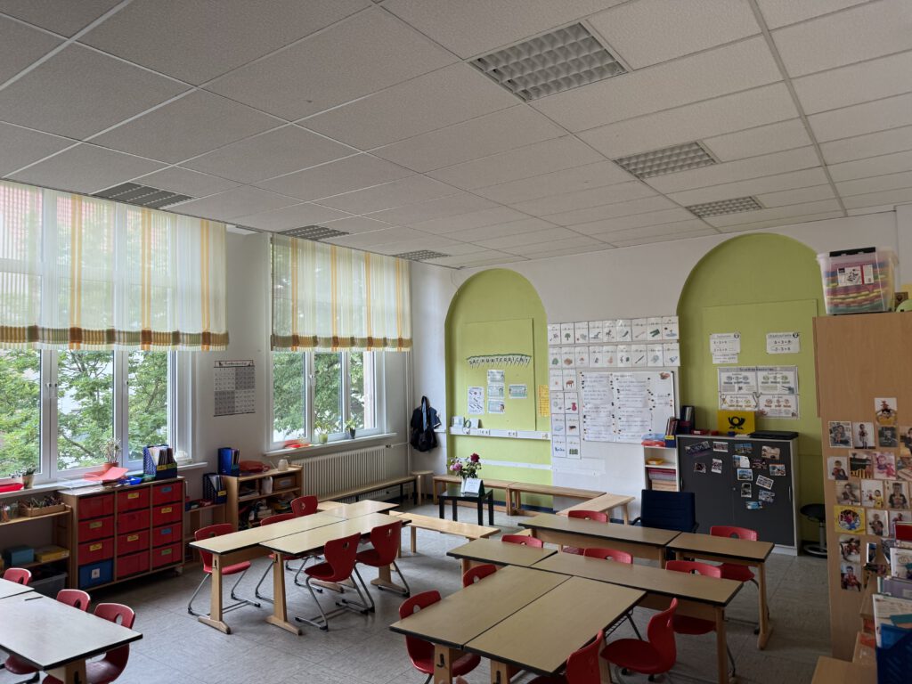 Innenaufnahme eines bunt gestalteten Klassenzimmers in der Karlschule Paderborn mit leeren Tischen und Stühlen vor großen Fenstern.